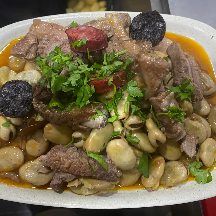 Um prato de carne com feijão, enchidos e coentros