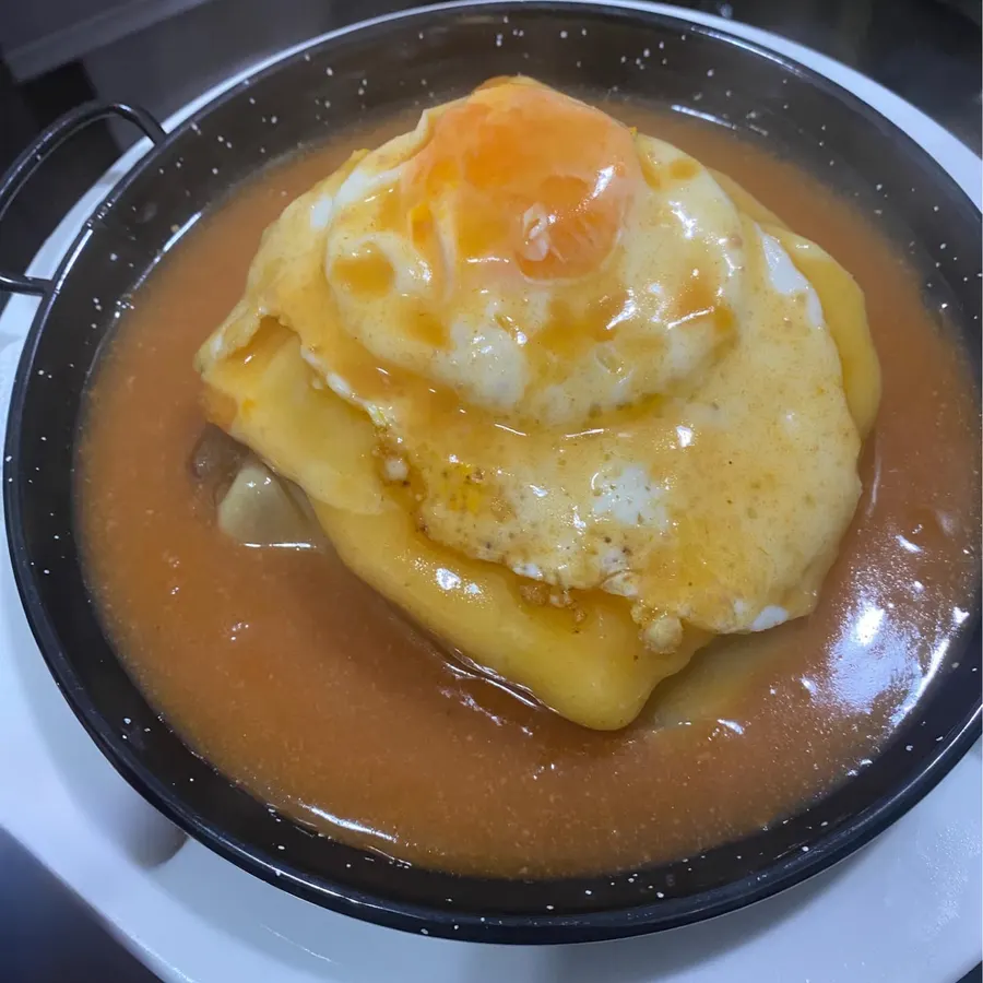 Uma francesinha com ovo, no prato de barro